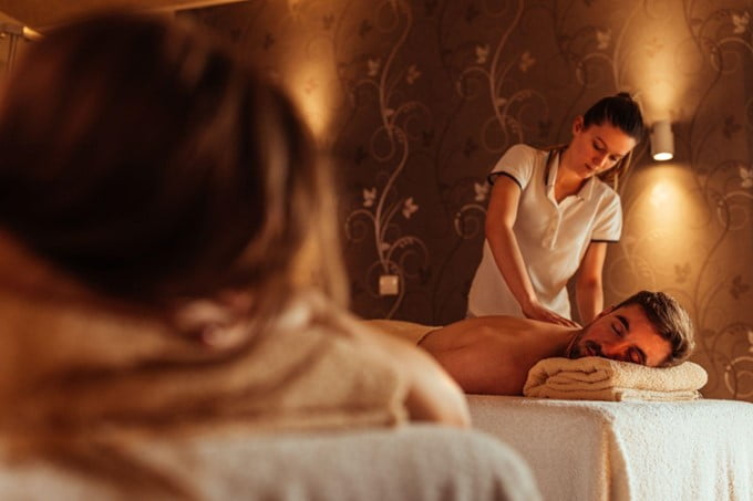 Um homem recebe uma massagem tântrica relaxante de um terapeuta em uma sala de spa pouco iluminada, criando uma atmosfera de profunda tranquilidade.